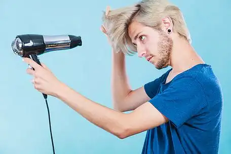 金发男人拿着吹风机和梳子在蓝色上创造新发型.有吹风机的时髦人