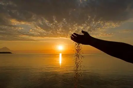 倒计时器生命时间流逝的概念.人手在日出背景上倒沙照片