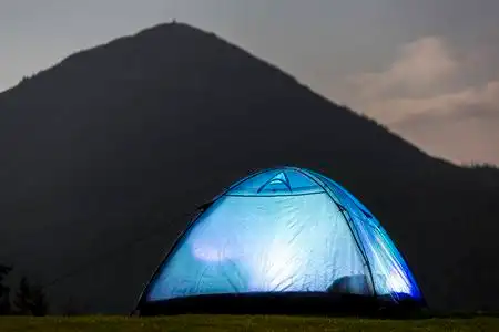 旅游远足帐篷明亮地从里面在绿色草谷在松树之下在深蓝色多云天空之下