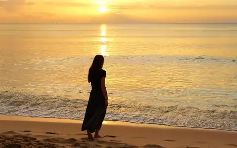 孤独的女孩在夕阳下漫步在沙滩上照片