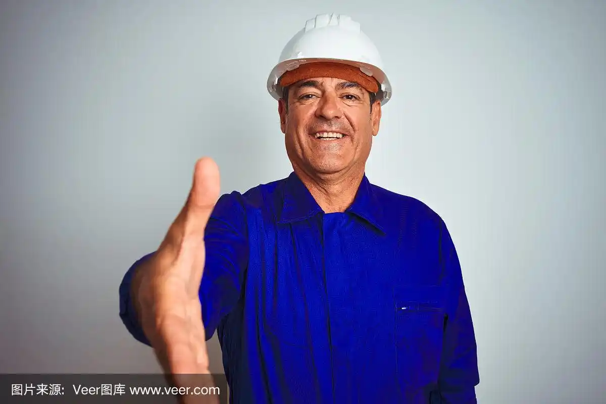 英俊的中年工人穿着制服和头盔在孤立的白色背景微笑友好地提供握手