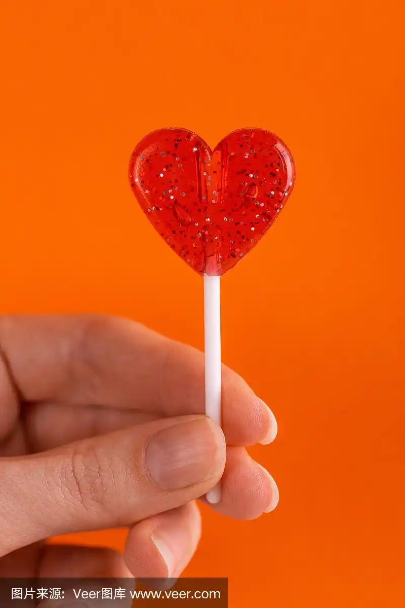 甜美的鲜红色棒棒糖在女人的手在明亮的橙色背景