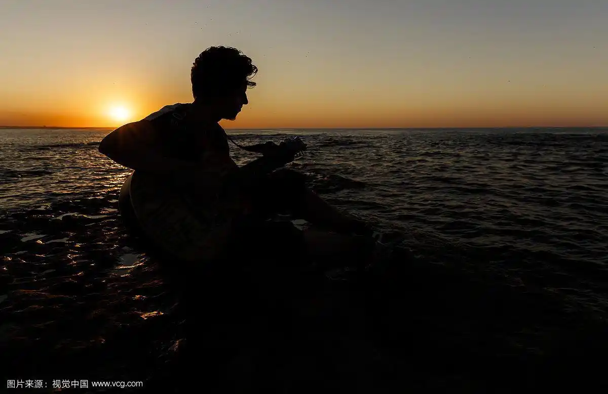 日落时分沙滩上弹吉他的男人