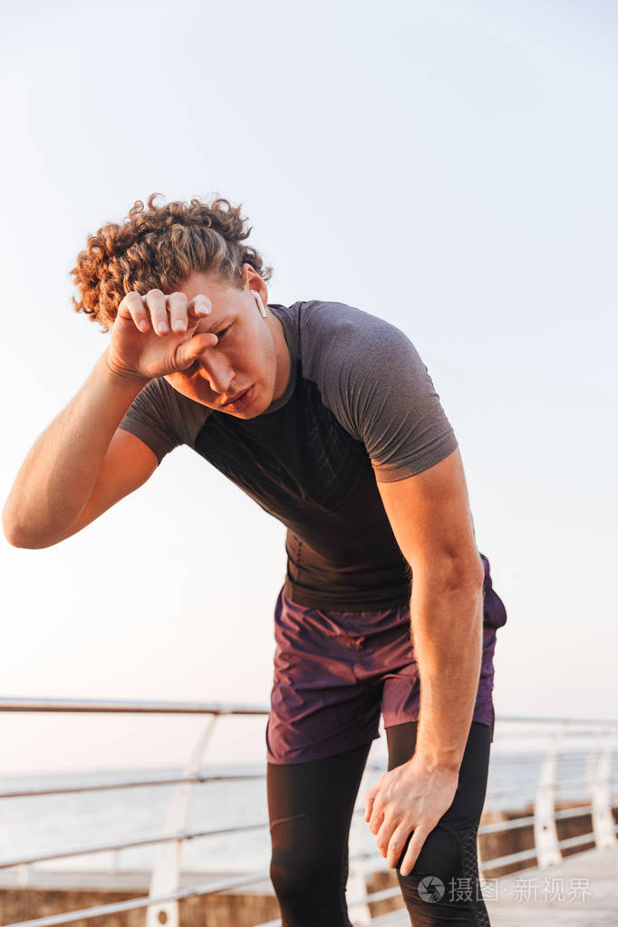 在海滩锻炼后休息的出汗运动员的肖像, 听音乐与耳机