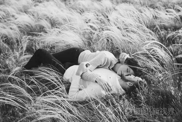 幸福的年轻情侣躺在羽毛草里从上面笑着拥抱着黑白风格