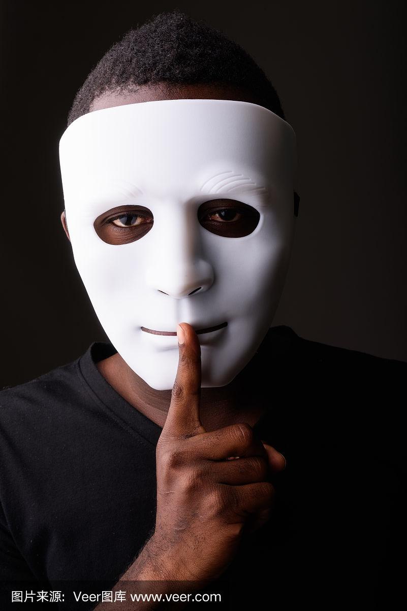 摄影棚拍摄的年轻非洲黑人男子在黑暗的房间里戴着面具,把手指放在