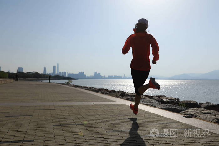 健身女运动员在阳光明媚的海岸公路上跑步