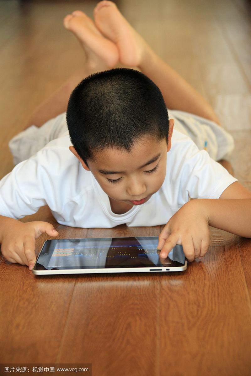 东方男孩趴在地板玩电脑