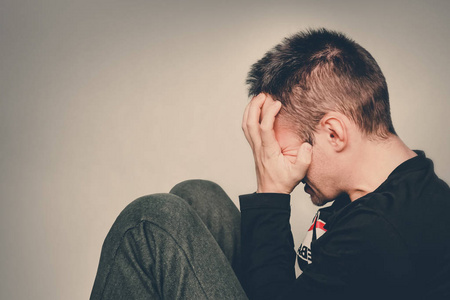 疲劳的男人一个男人哭了.忧郁的年轻人坐在地板上牵着手.