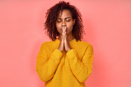 照片中美丽的年轻黑人妇女双手合十祈祷,闭上眼睛,享受祥和的气氛,有