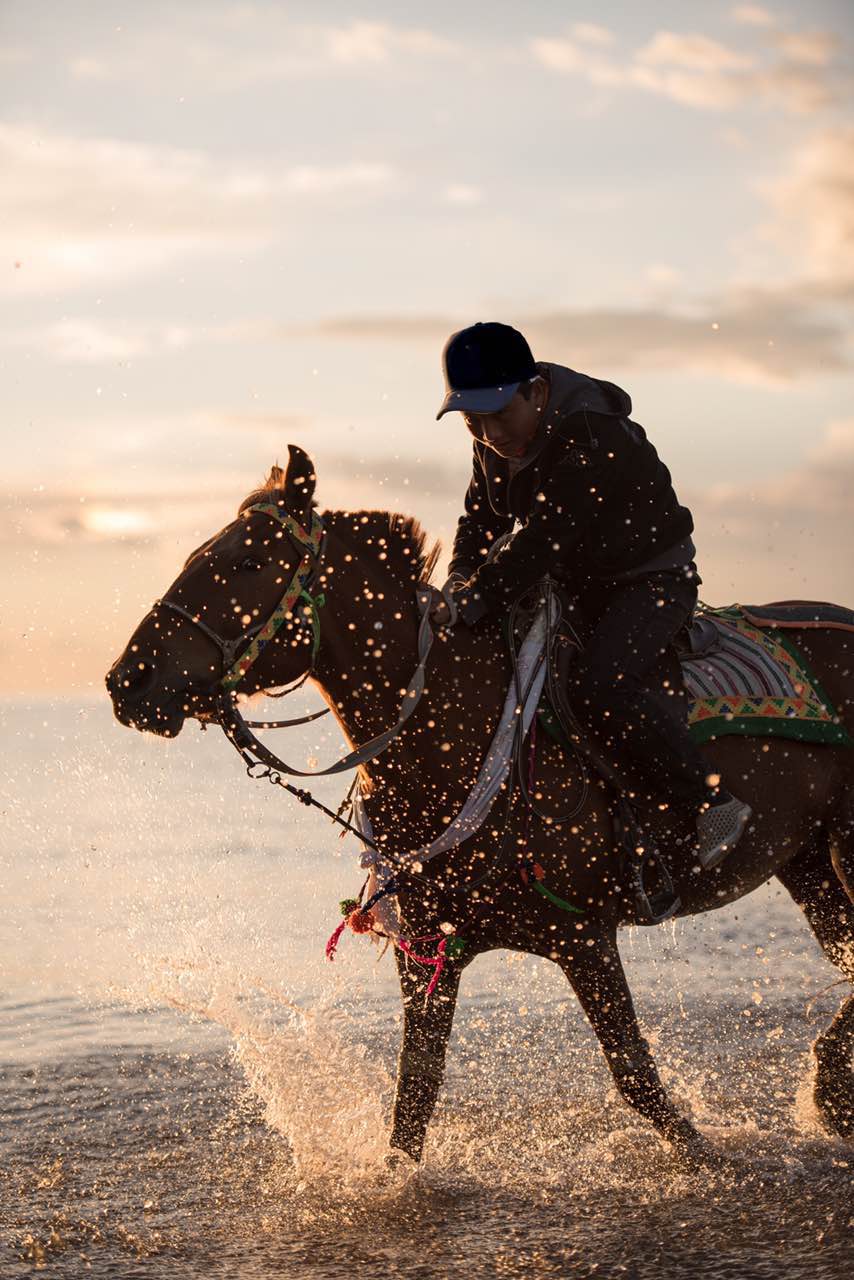 夕阳西下,一位少年骑马奔入湖边,马儿跑起来溅起的水花很