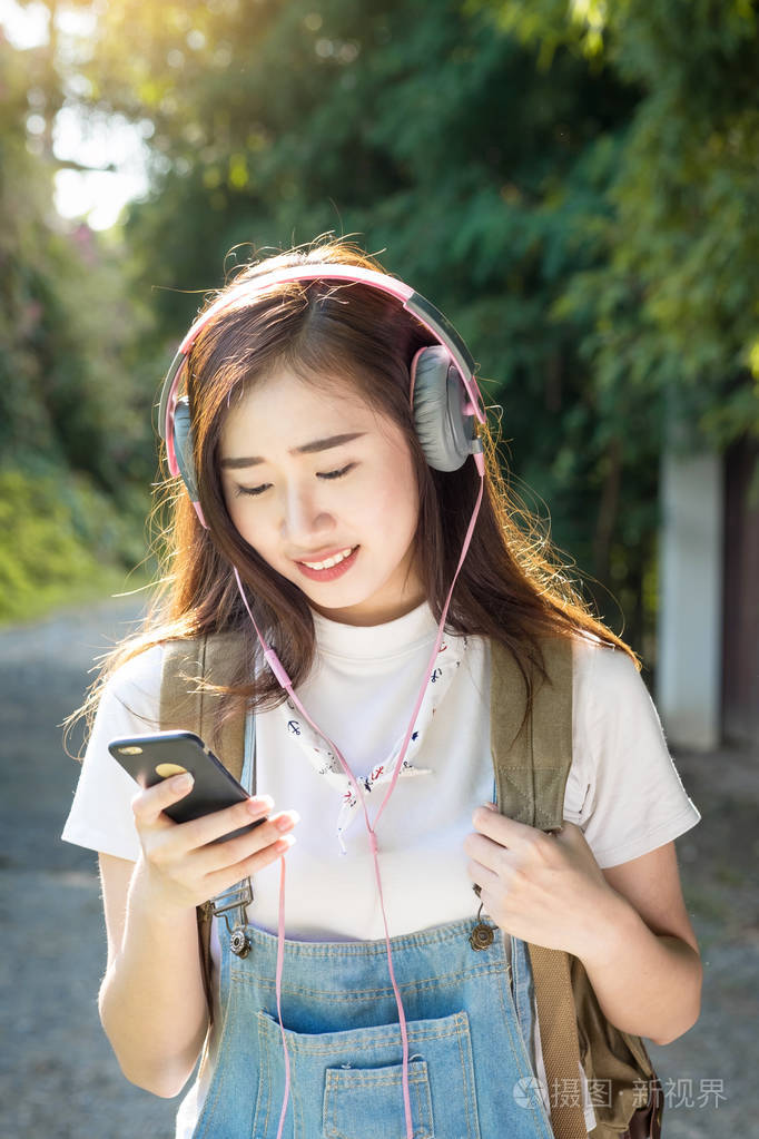 年轻的亚洲时髦戴耳机听音乐通过