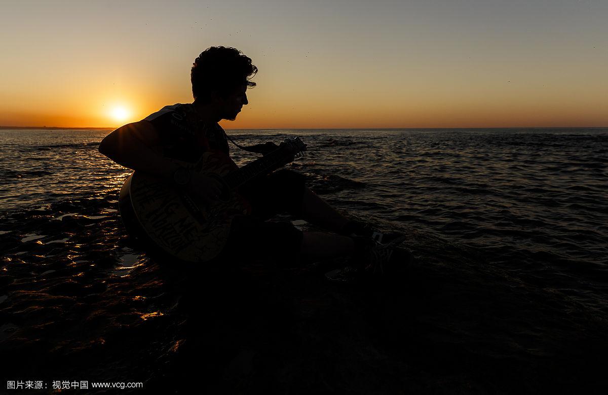 日落时分沙滩上弹吉他的男人