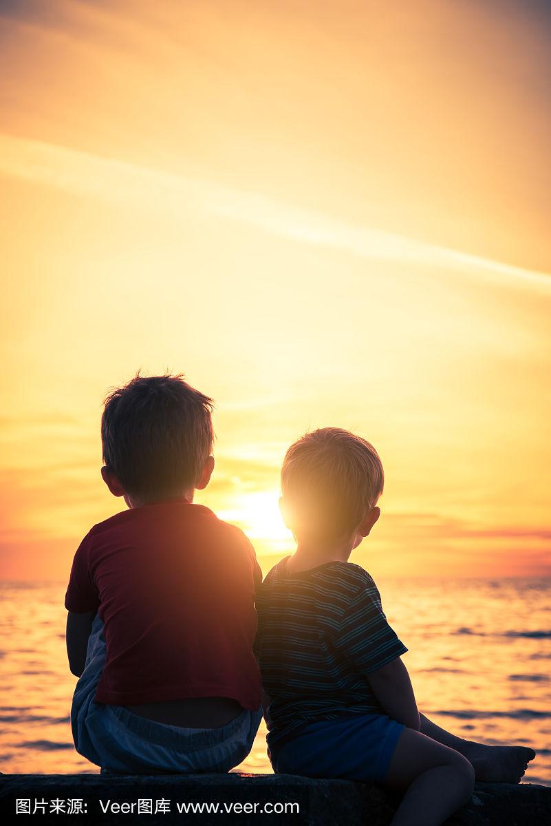 夕阳西下时,两个男孩坐在海滩的岩石上
