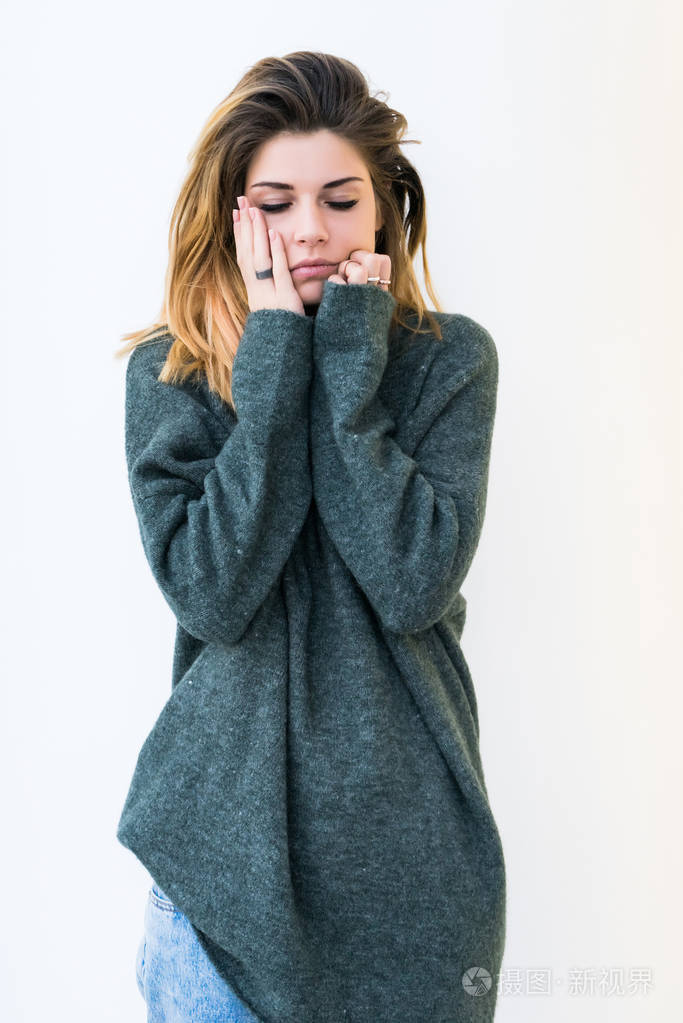 一个可爱的女孩,在大的灰色毛衣和茂密的头发,捂着
